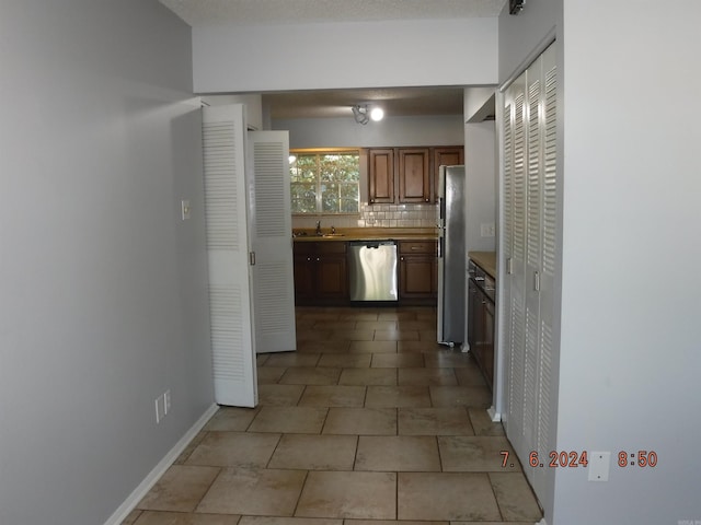 kitchen with appliances with stainless steel finishes, backsplash, light tile patterned floors, and sink