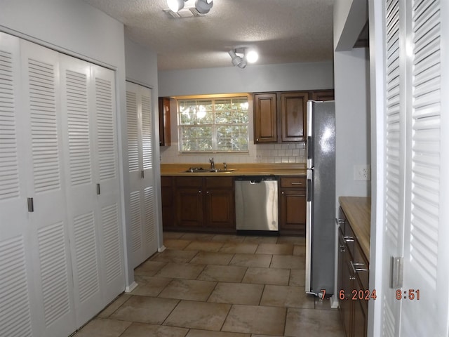 kitchen with sink, tile patterned flooring, a textured ceiling, appliances with stainless steel finishes, and tasteful backsplash