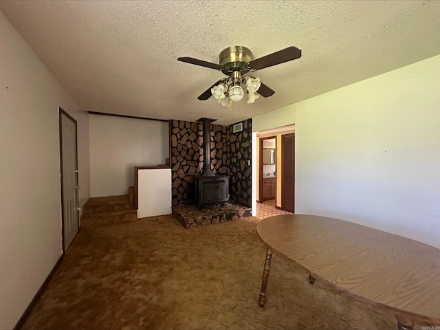 unfurnished living room with carpet flooring, ceiling fan, a wood stove, and a textured ceiling