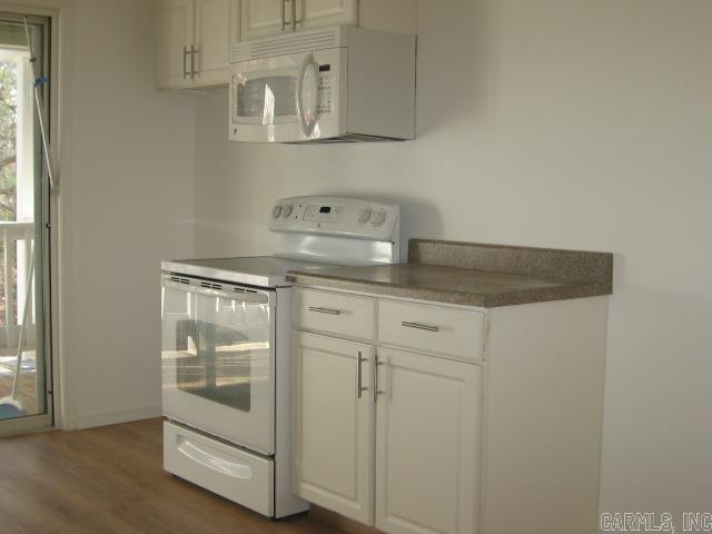 kitchen with white cabinets, dark hardwood / wood-style flooring, and white appliances