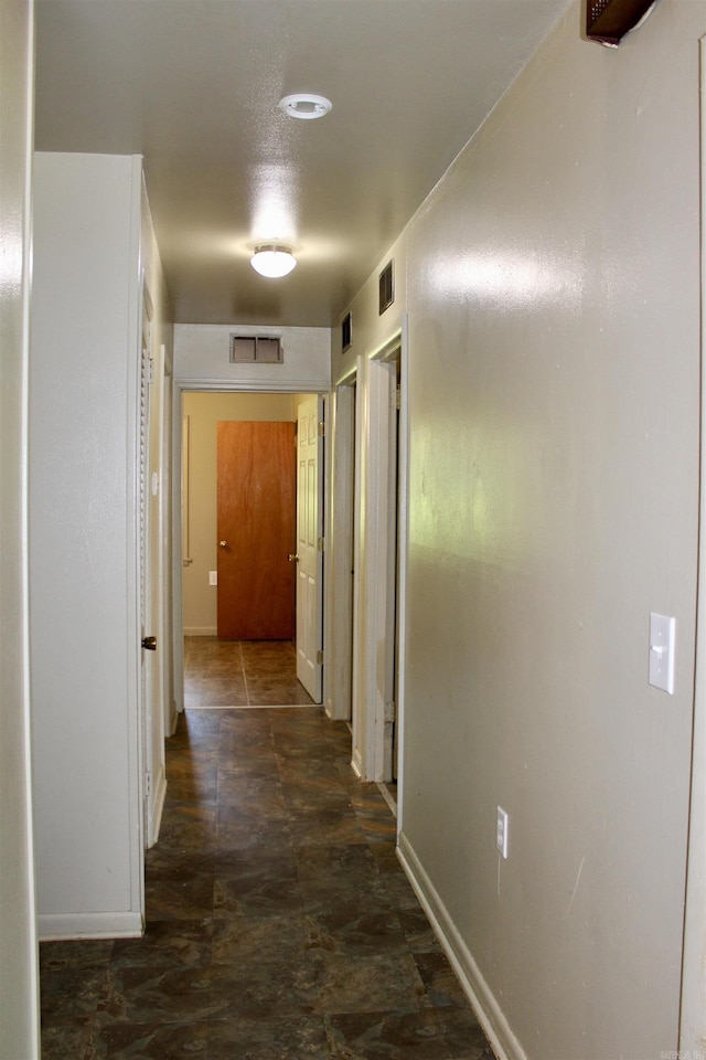 hall with stone finish floor, visible vents, and baseboards