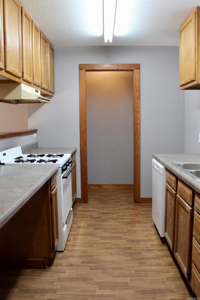 kitchen with white appliances, under cabinet range hood, light wood finished floors, and light countertops