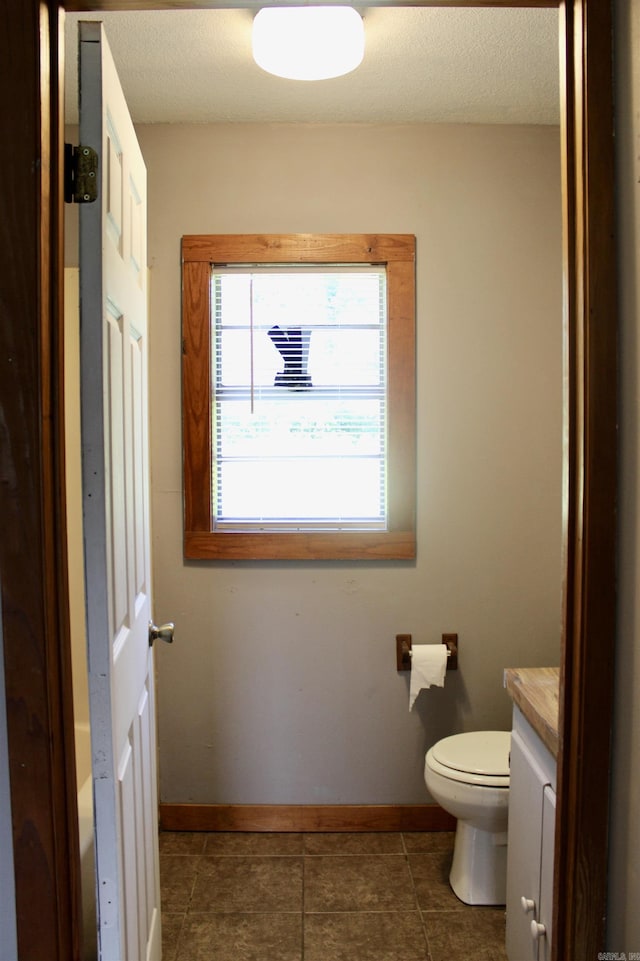 bathroom with a textured ceiling, vanity, toilet, and baseboards