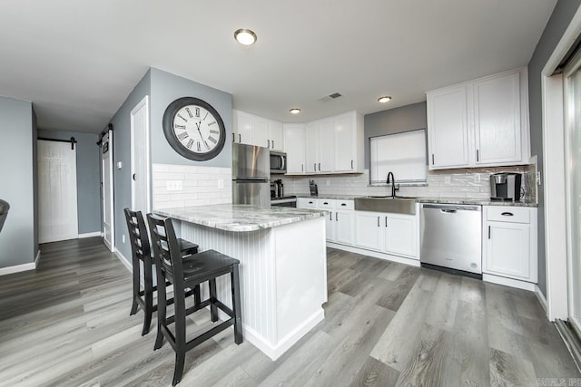 kitchen with stainless steel appliances, light wood-type flooring, a barn door, sink, and white cabinets