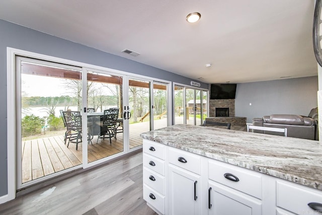 kitchen featuring white cabinetry, light hardwood / wood-style flooring, a fireplace, and light stone countertops