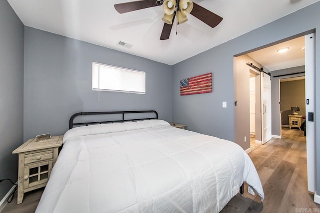 bedroom featuring ceiling fan, a barn door, and light hardwood / wood-style floors