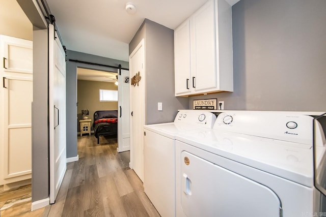 laundry room with ceiling fan, washing machine and clothes dryer, light wood-type flooring, a barn door, and cabinets