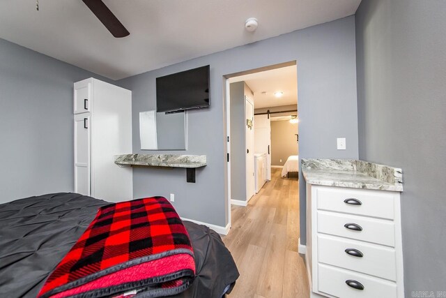 bedroom featuring a barn door, light wood-type flooring, and ceiling fan