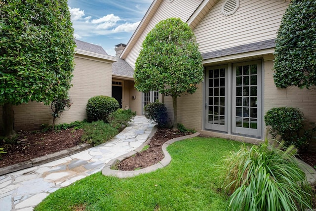 doorway to property with brick siding, roof with shingles, and a lawn