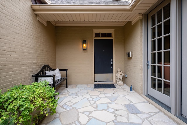 view of exterior entry with a shingled roof and brick siding