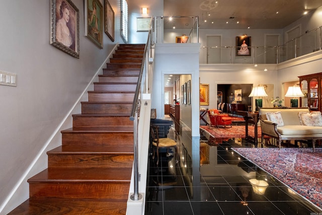 stairs with a towering ceiling, granite finish floor, and baseboards