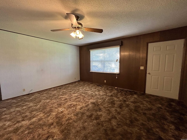 carpeted empty room with a textured ceiling, ceiling fan, and wooden walls