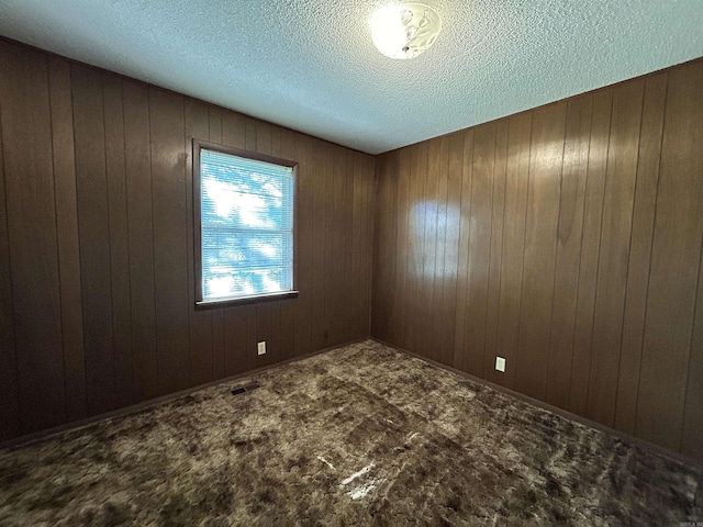 carpeted spare room featuring wooden walls and a textured ceiling