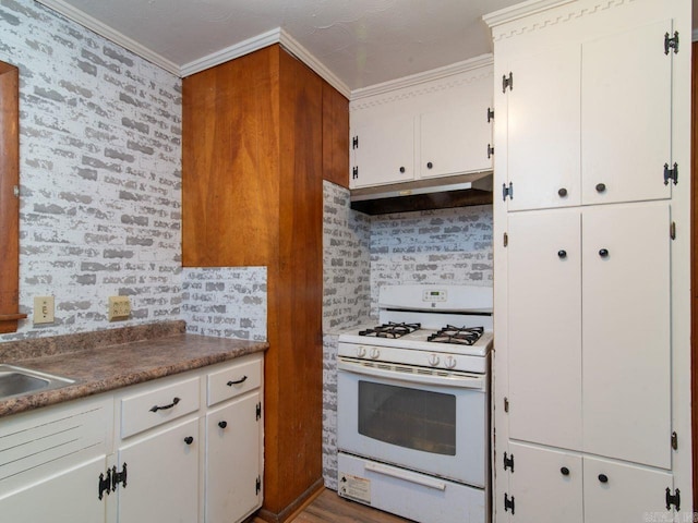 kitchen with backsplash, white gas range, ornamental molding, hardwood / wood-style flooring, and white cabinets