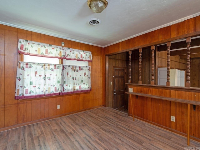 empty room featuring hardwood / wood-style flooring, crown molding, and wood walls