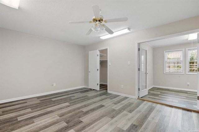 unfurnished bedroom featuring hardwood / wood-style floors, a walk in closet, a closet, and ceiling fan