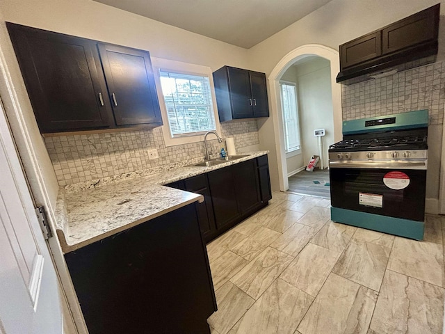 kitchen with gas range, light stone counters, sink, and decorative backsplash