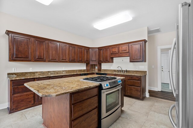 kitchen featuring dark brown cabinets, stainless steel appliances, a kitchen island, and light tile floors