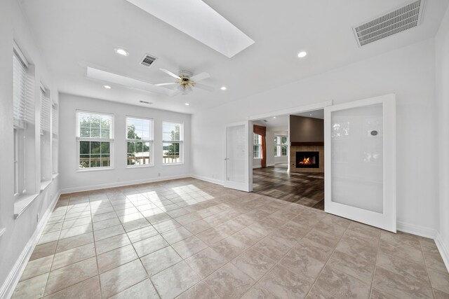 empty room with ceiling fan, light hardwood / wood-style flooring, and a skylight