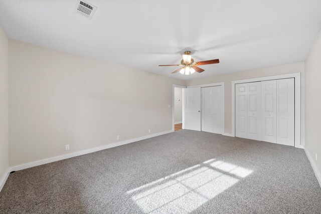 unfurnished bedroom with ceiling fan, carpet floors, and multiple closets