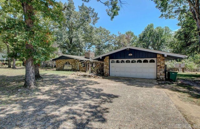 view of front of house featuring driveway, stone siding, a garage, and a chimney