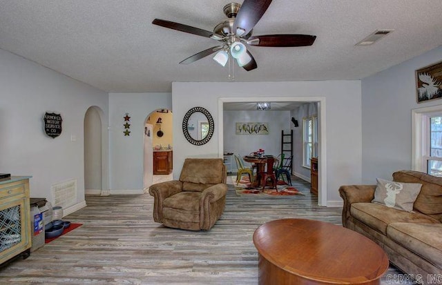 living room featuring baseboards, visible vents, arched walkways, wood finished floors, and a textured ceiling