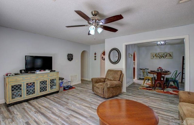 living room with a ceiling fan, arched walkways, a textured ceiling, and wood finished floors