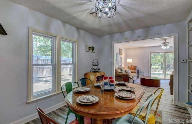 dining area with baseboards, a textured ceiling, visible vents, and wood finished floors