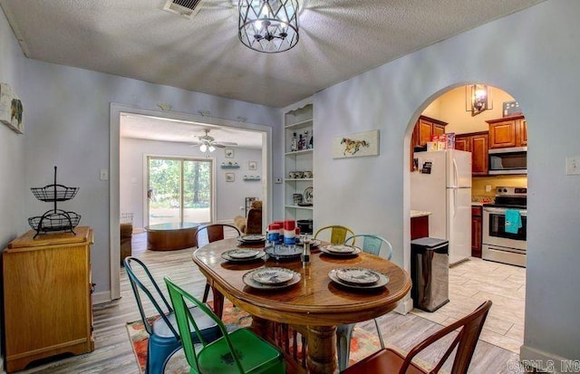 dining room featuring arched walkways, a textured ceiling, and light wood-style floors