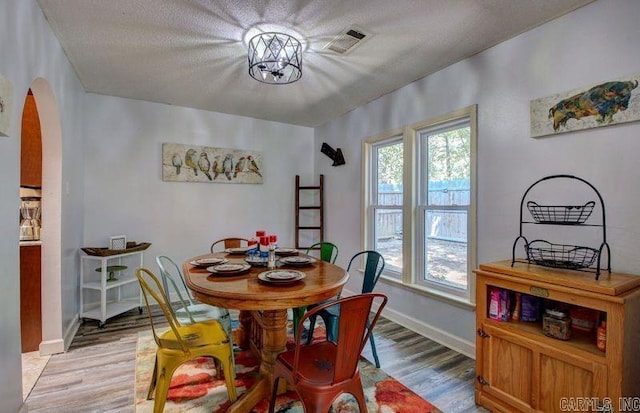 dining area with light wood-style floors, arched walkways, visible vents, and baseboards