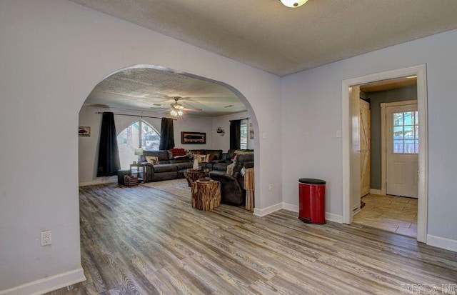 living area with baseboards, a textured ceiling, arched walkways, and wood finished floors