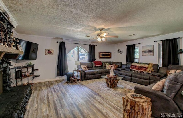 living area with a fireplace with raised hearth, crown molding, visible vents, and wood finished floors