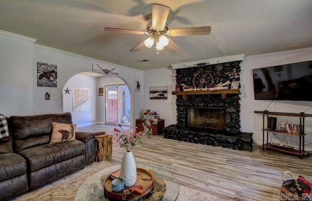 living room featuring arched walkways, wood finished floors, crown molding, a stone fireplace, and a textured ceiling