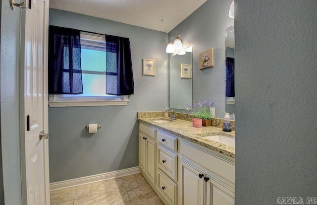 full bath with double vanity, a textured ceiling, baseboards, and a sink