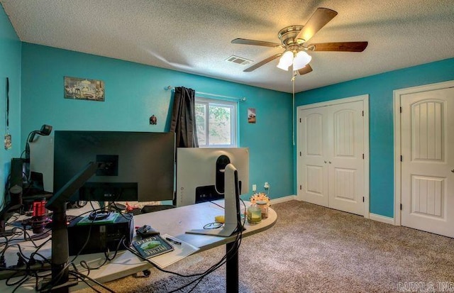 carpeted home office featuring a ceiling fan, visible vents, a textured ceiling, and baseboards