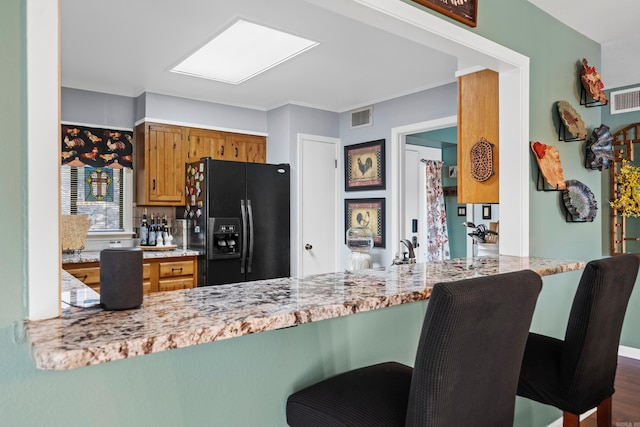 kitchen with kitchen peninsula, a kitchen breakfast bar, dark hardwood / wood-style flooring, and black refrigerator with ice dispenser