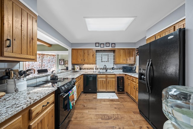 kitchen with light stone countertops, sink, beverage cooler, black appliances, and light wood-type flooring