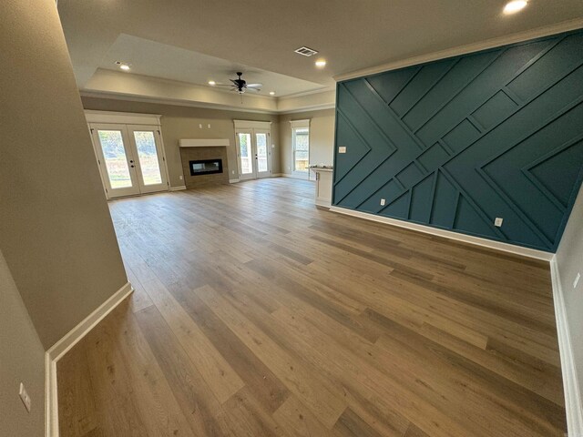 unfurnished living room with ceiling fan, a raised ceiling, wood-type flooring, and french doors