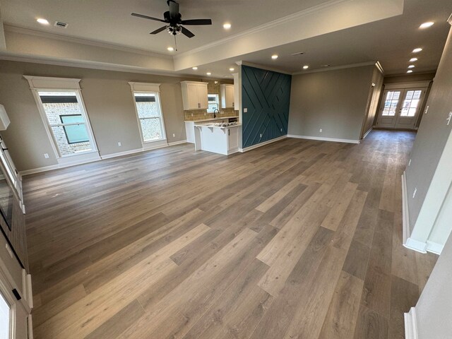 unfurnished living room with plenty of natural light, ceiling fan, wood-type flooring, and ornamental molding