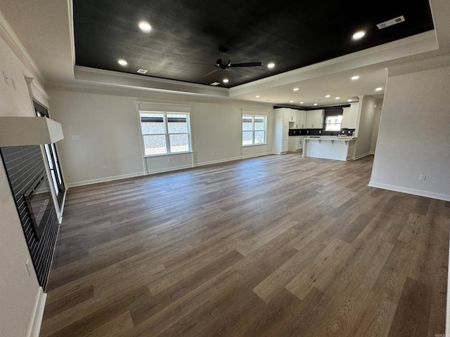 unfurnished living room with ceiling fan, dark hardwood / wood-style flooring, crown molding, and a raised ceiling