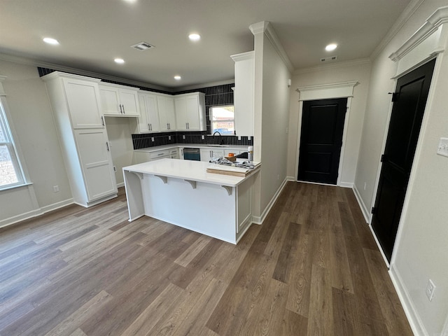 kitchen featuring kitchen peninsula, white cabinetry, a breakfast bar area, light wood-type flooring, and crown molding