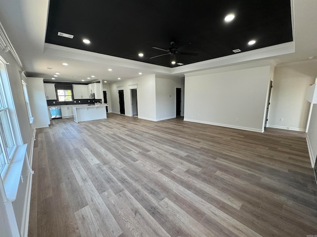 unfurnished living room with ornamental molding, ceiling fan, a tray ceiling, and light hardwood / wood-style flooring