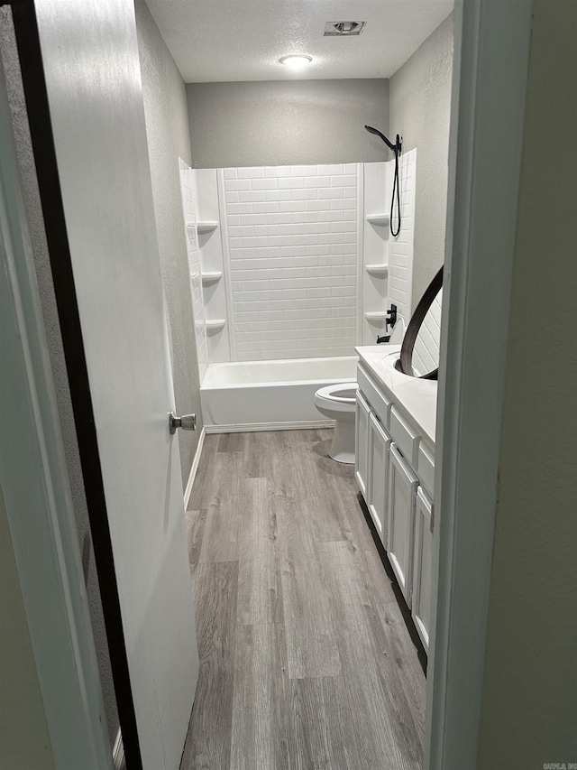 full bathroom featuring vanity, a textured ceiling, hardwood / wood-style floors, toilet, and tiled shower / bath