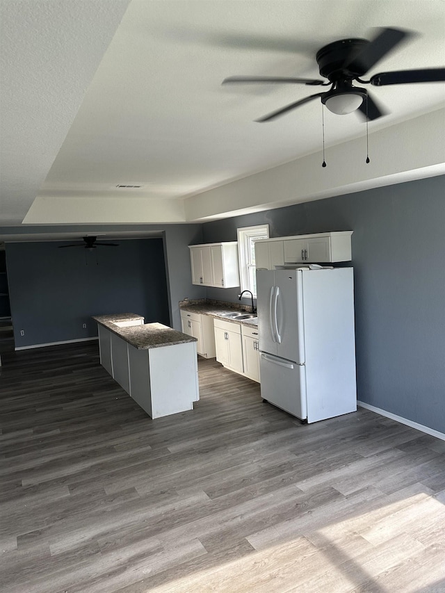 kitchen with white refrigerator, sink, hardwood / wood-style flooring, a kitchen island, and white cabinetry