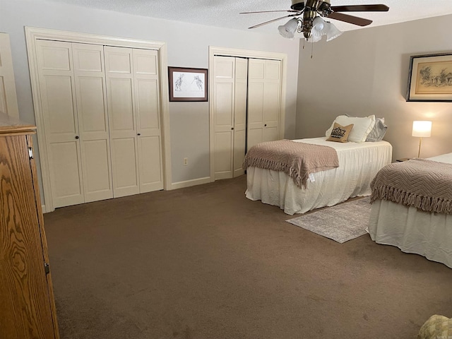 bedroom with dark colored carpet, ceiling fan, a textured ceiling, and two closets