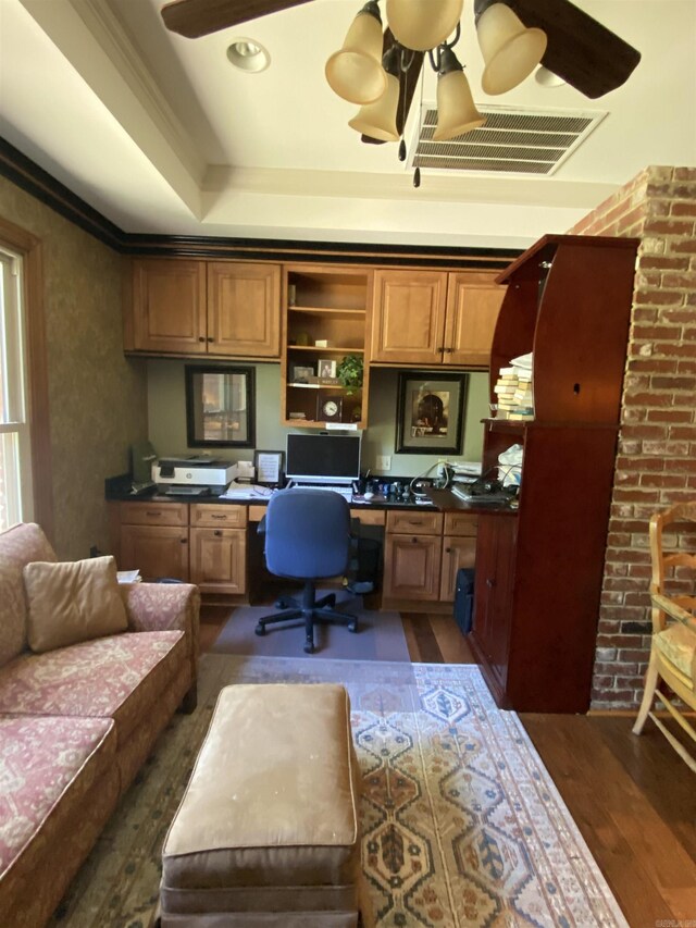 office featuring a raised ceiling, dark hardwood / wood-style flooring, built in desk, and crown molding