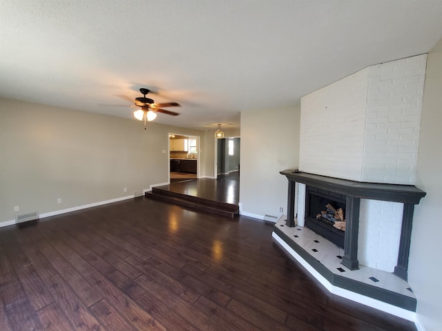 unfurnished living room featuring a fireplace, a textured ceiling, ceiling fan, and dark wood-type flooring