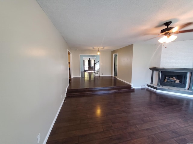 unfurnished living room featuring ceiling fan, a large fireplace, dark wood-type flooring, and a textured ceiling