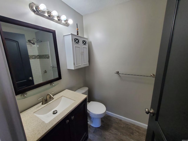 bathroom with vanity, toilet, a textured ceiling, tiled shower, and wood-type flooring