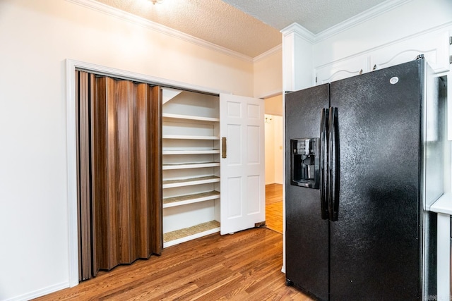 kitchen with black refrigerator with ice dispenser, ornamental molding, a textured ceiling, light hardwood / wood-style floors, and white cabinetry